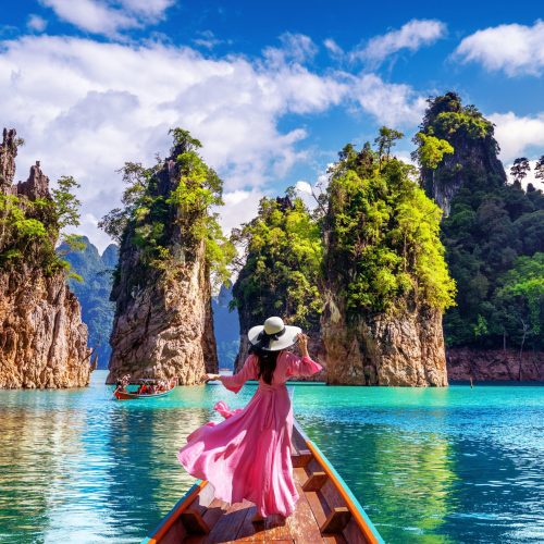 Beautiful girl standing on the boat and looking to mountains in Ratchaprapha Dam at Khao Sok National Park, Surat Thani Province, Thailand.